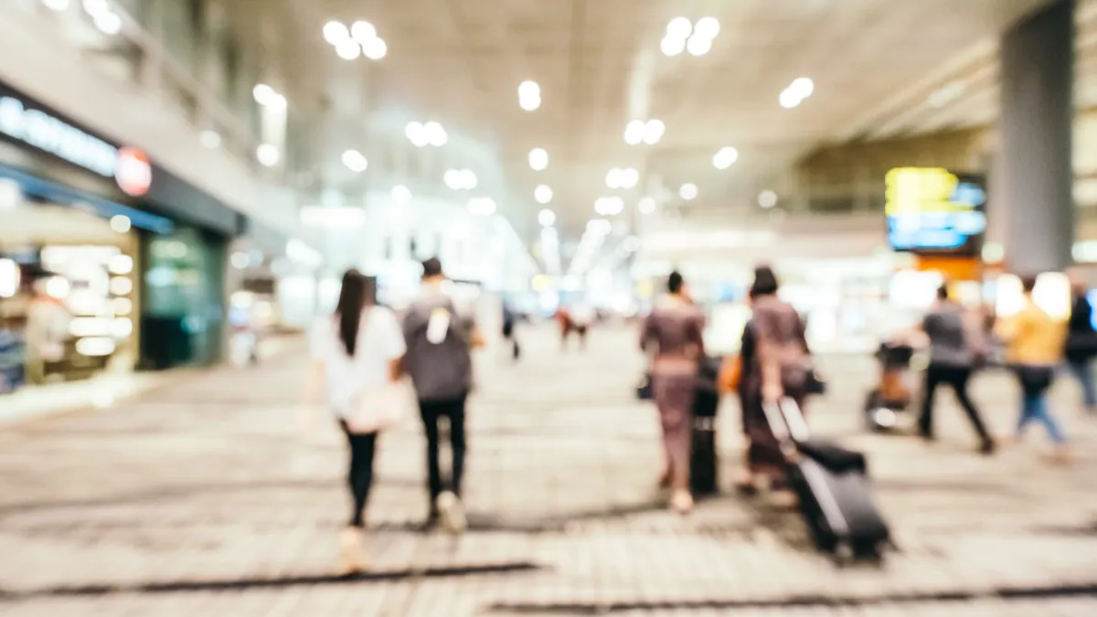 Travellers with suitcases walk through a bright airport terminal hall.