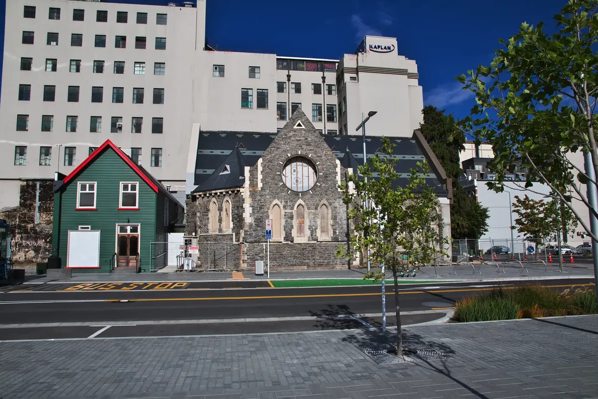 Una iglesia de piedra y una casita de madera verde en una calle del centro de Christchurch
