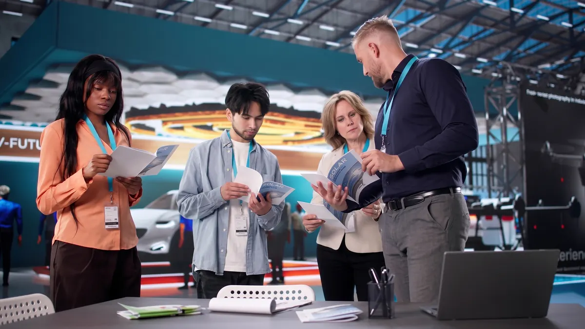 Ein Team sieht sich an einem Messestand Broschüren an