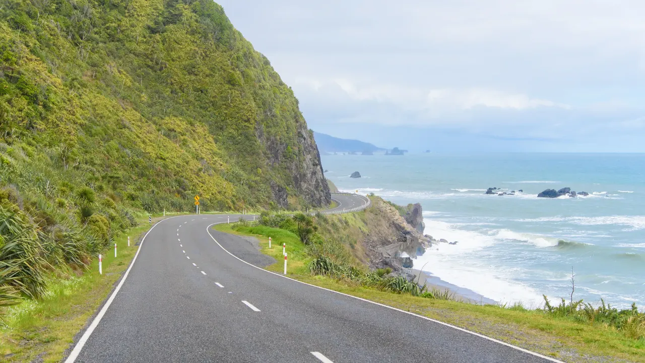 Une route longeant une falaise couverte de végétation au-dessus d'une côte rocheuse. Une option à terre garde la journée utile quand le bateau ne peut pas sortir.