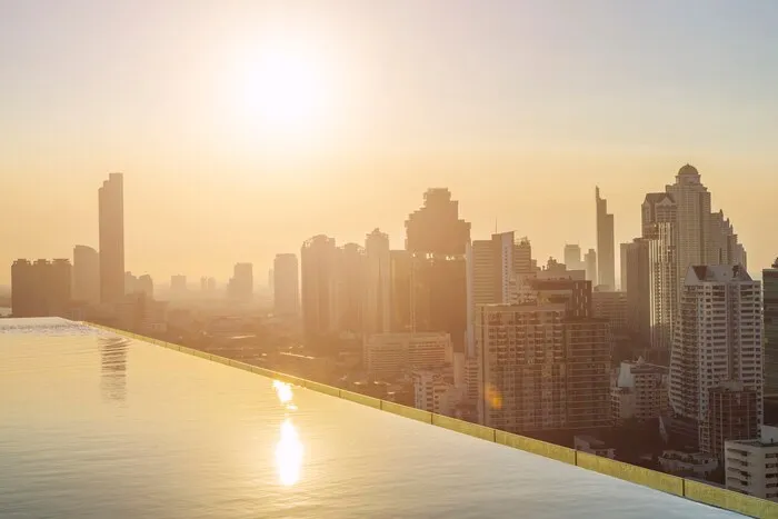 Une piscine sur un toit au-dessus des tours de Bangkok au coucher du soleil. Avec la chaleur de fin avril, un hôtel avec piscine se vend facilement.