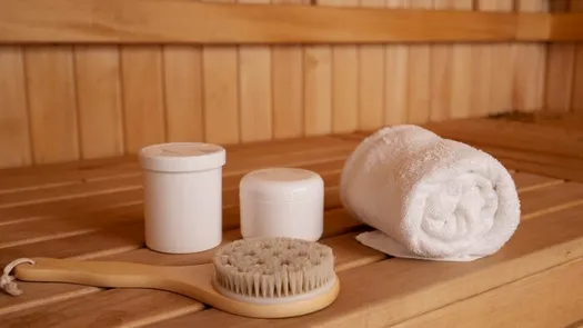 A wooden sauna bench with a rolled white towel and a bath brush.
