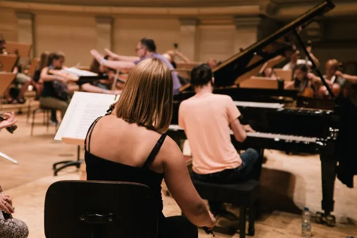 Musicians rehearsing with a grand piano on a concert stage.