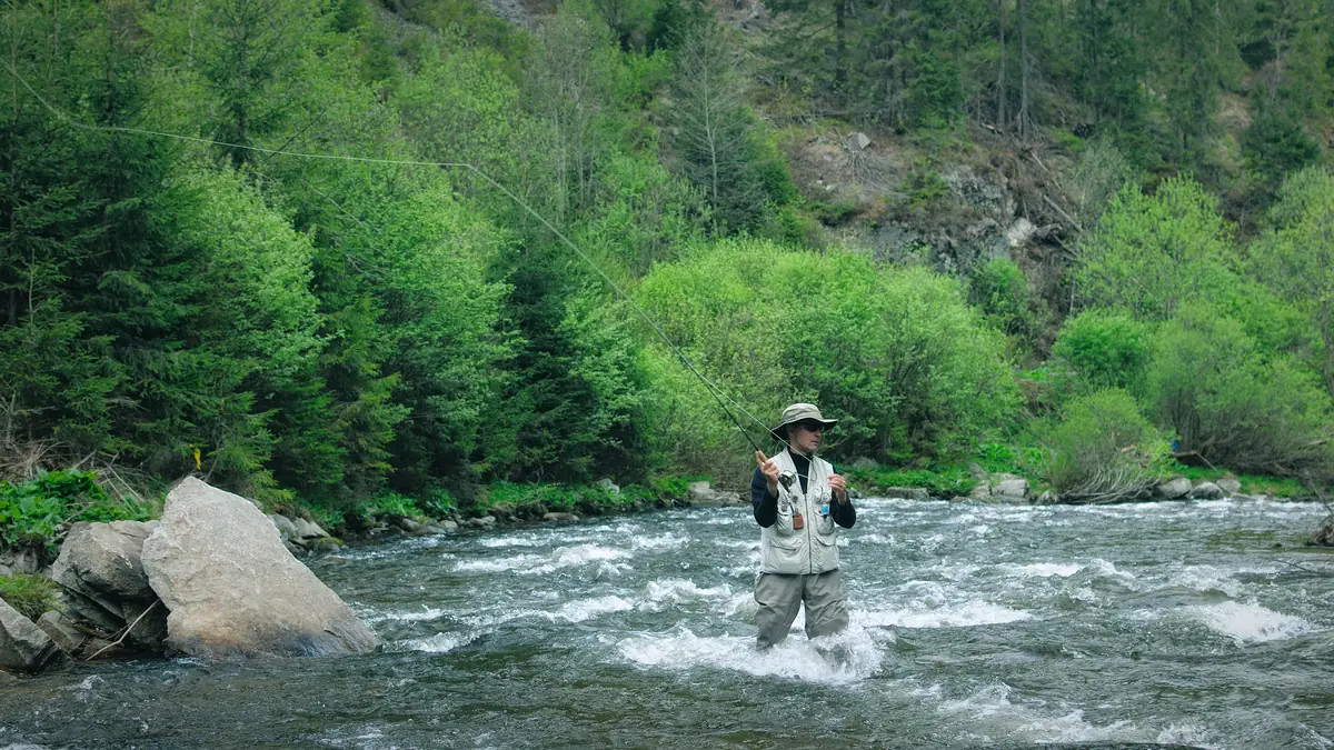 Un pescador lanzando de pie en un río de corriente rápida