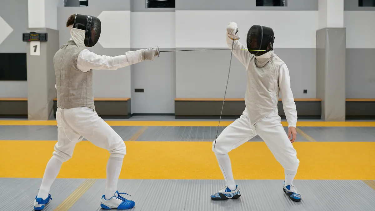 白いユニフォームとマスクを着けた2人のフェンシング選手が競技ピストで対戦する様子
