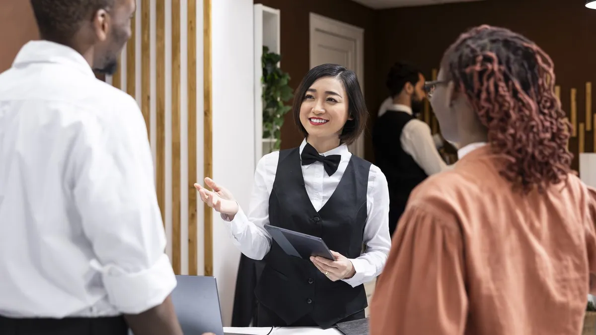 Hotel staff welcome arriving guests at a reception desk.