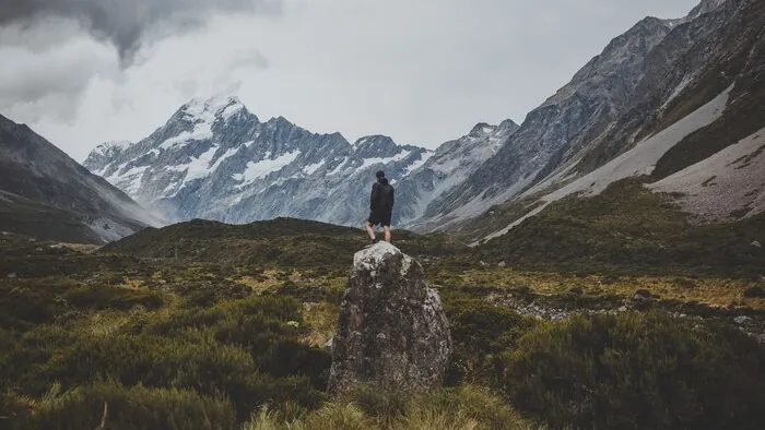 Ein Wanderer steht auf einem Felsblock in einem Bergtal