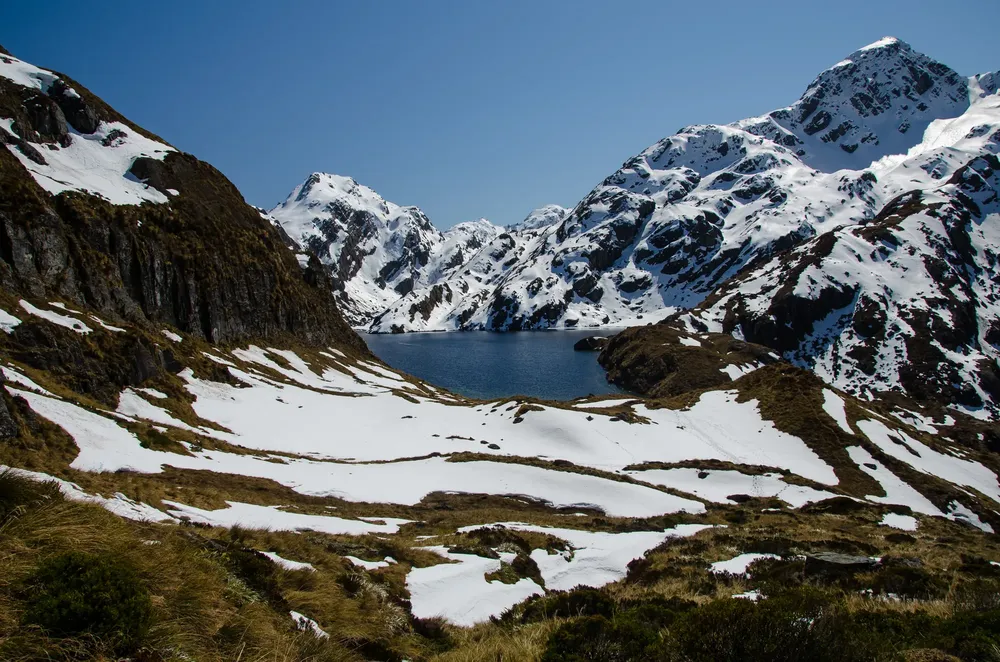 Snow on the mountains around an alpine lake, seen from the Routeburn Track