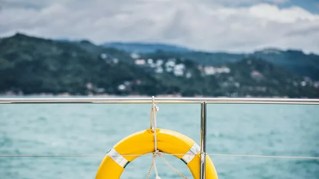 A yellow life ring hangs on a boat rail above open water.