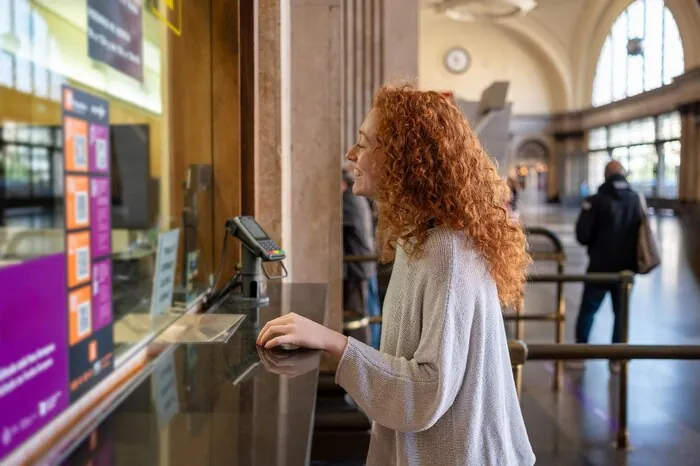 Uma viajante compra um bilhete no guiché de uma estação: comprar a entrada local a local é o atrito que os passes digitais querem eliminar.