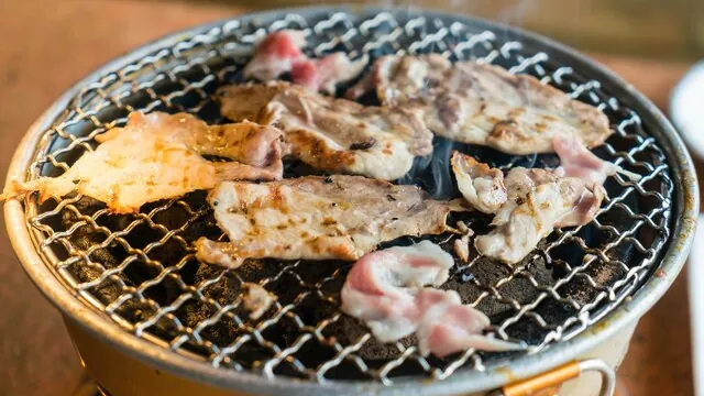Fatias de carne a grelhar numa grelha redonda a carvão.
