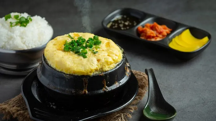 Un almuerzo coreano de huevo al vapor en olla de piedra caliente con arroz y guarniciones.