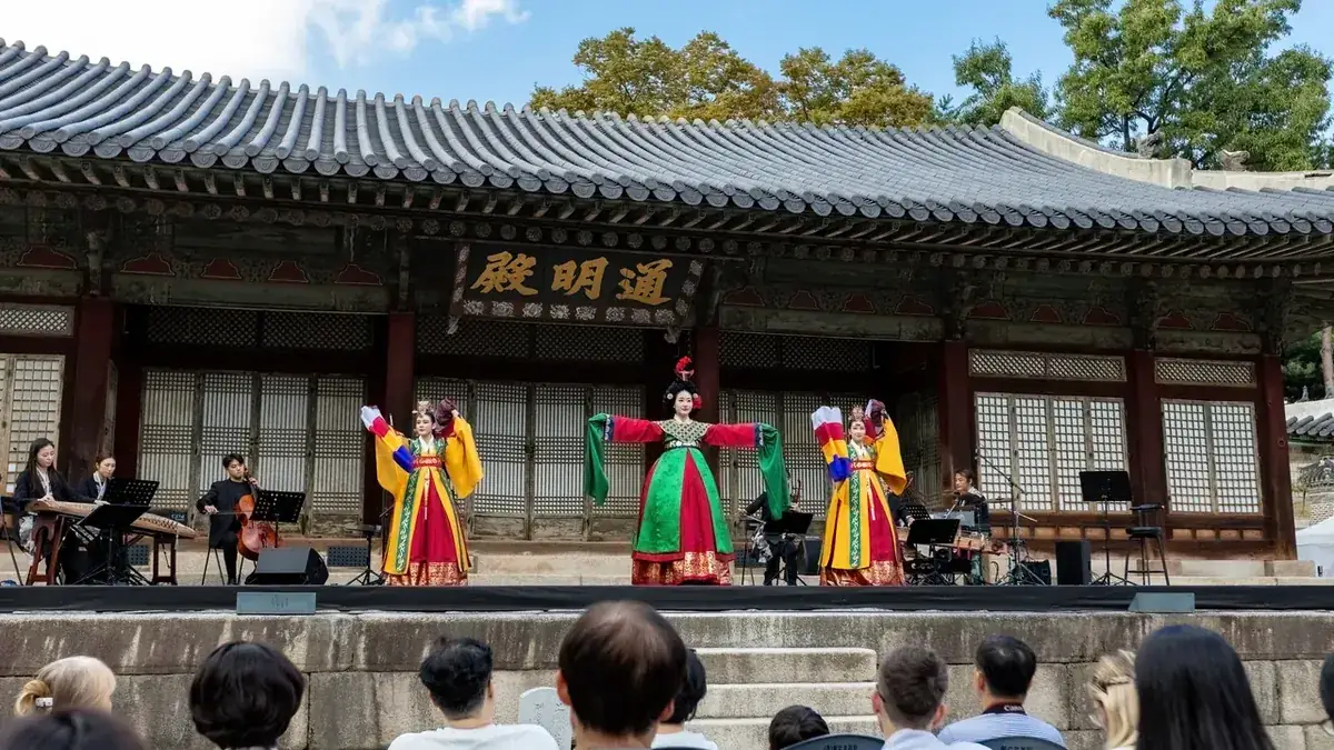 Tänzerinnen in Hanbok treten auf einer Bühne vor einer Palasthalle in Seoul auf, während Besucher zusehen. Eine Vorführung oder ein Tanzkurs gibt einem K-Kultur-Tag einen praktischen Teil.