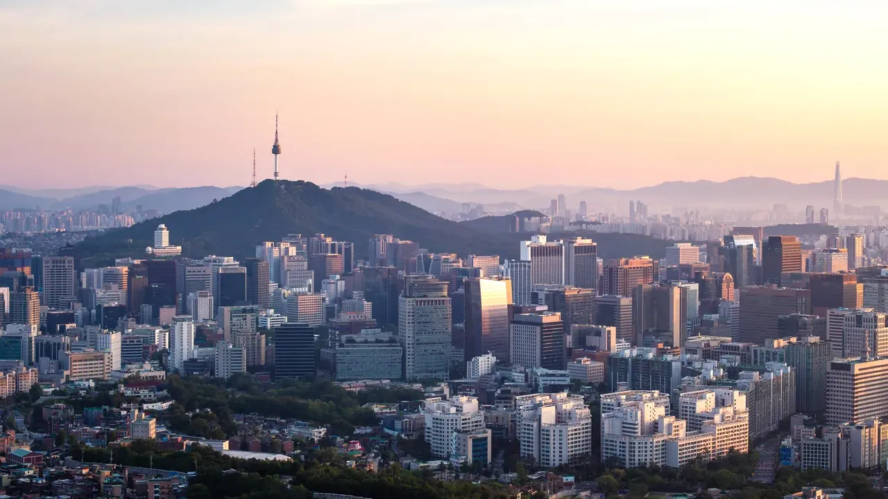 El centro de Seúl al amanecer, con la N Seoul Tower sobre el monte Namsan por encima de las torres de oficinas y montañas en la bruma al fondo.