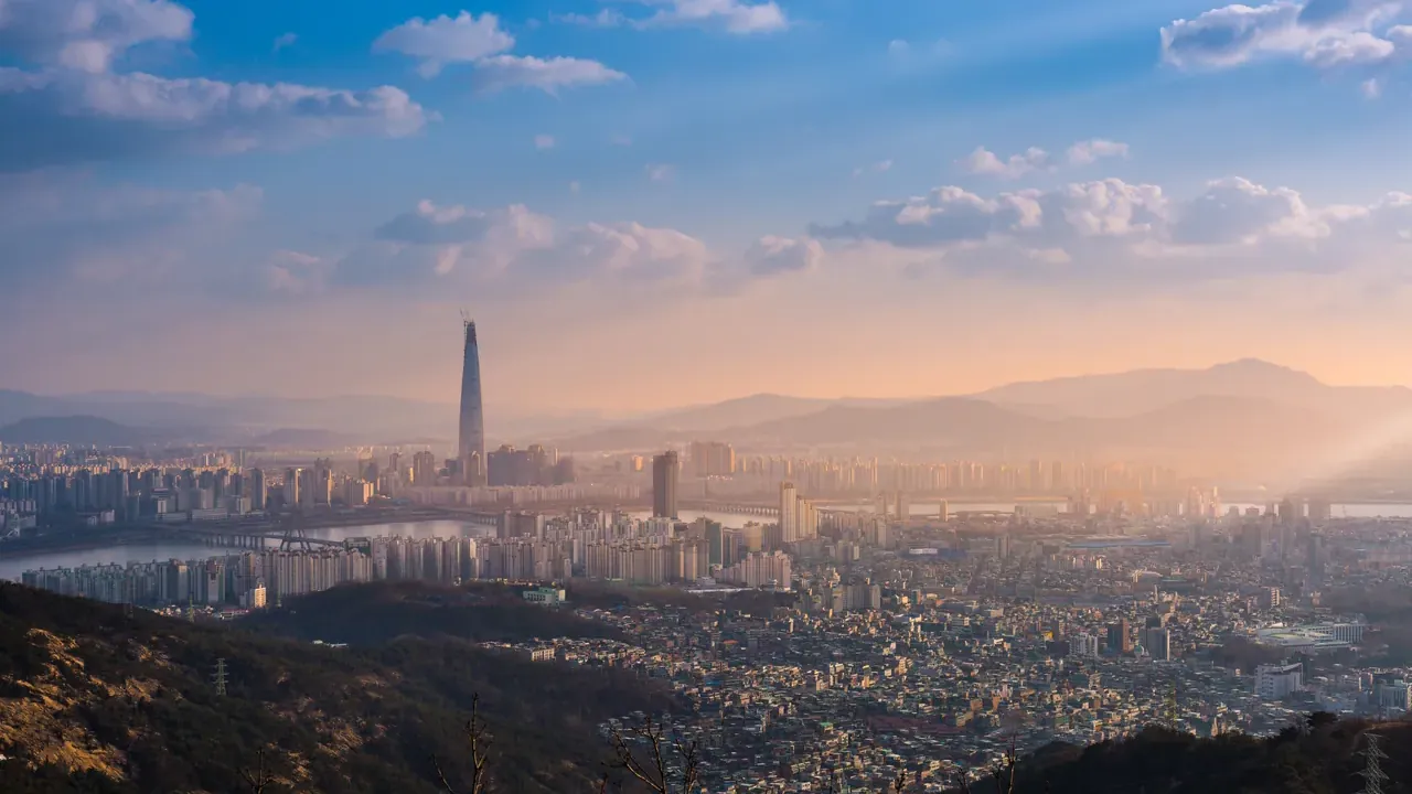 La Lotte World Tower y el río Han vistos desde una ladera al atardecer, con los bloques de viviendas del sudeste de Seúl debajo.