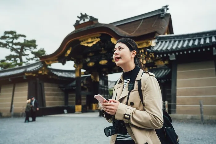 京都・二条城の門の前でスマートフォンのルートを確認する旅行者:お客様が市バスに乗るのは自由行動の時間です。