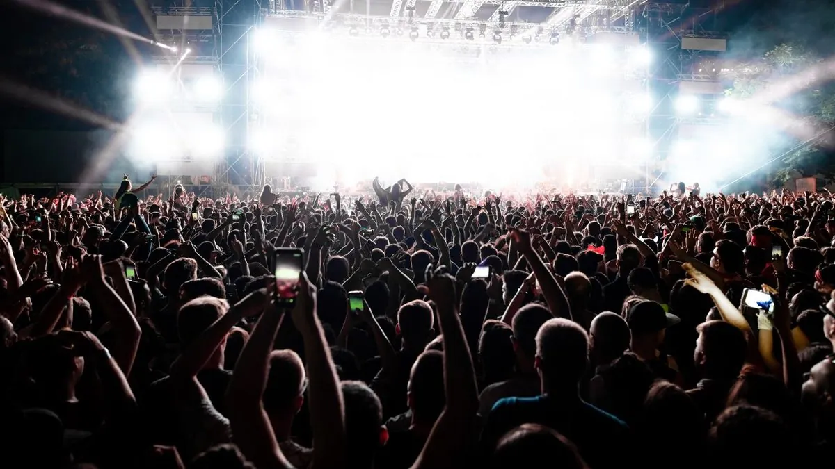 Un public de concert, mains et téléphones levés, sous de puissants projecteurs blancs.