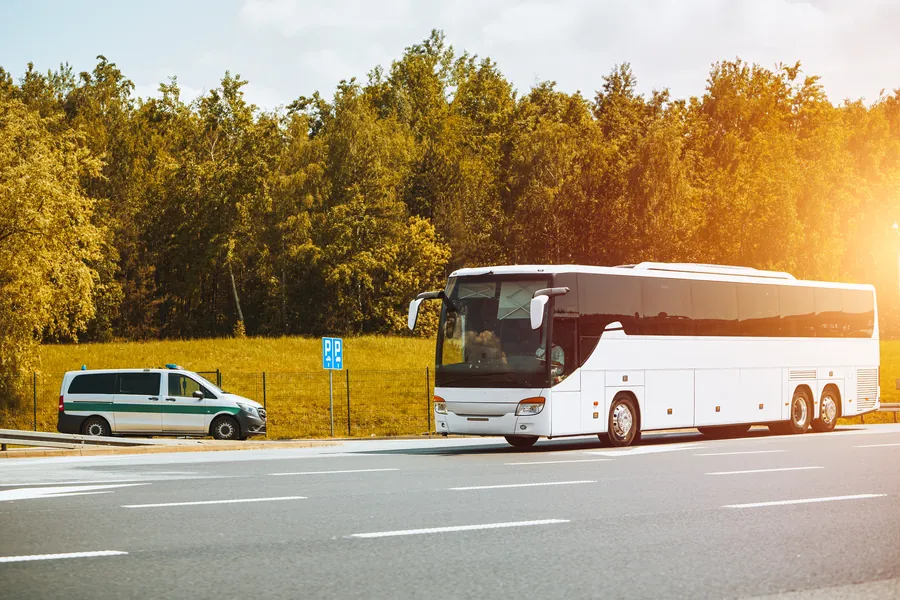 A white coach parked beside a road lined with trees