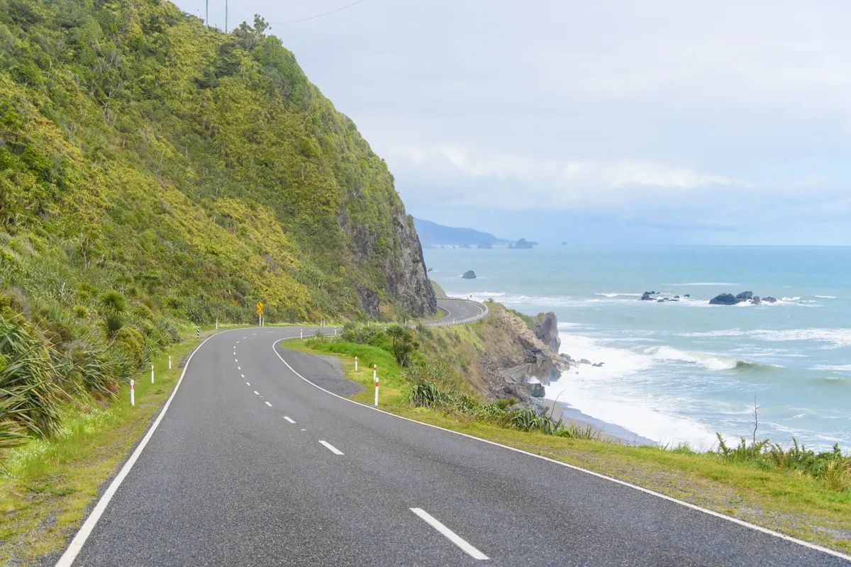 Uma estrada costeira a serpentear entre falésias verdes e o mar na Ilha Sul da Nova Zelândia