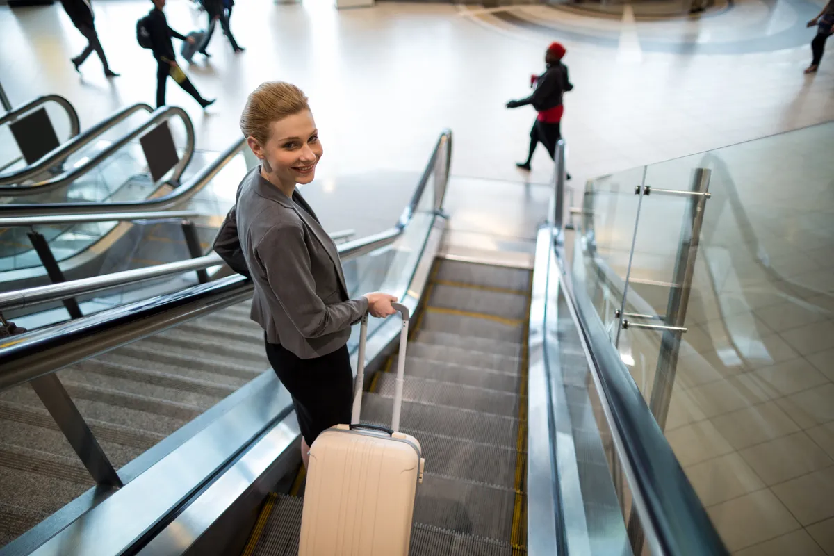 Um viajante com uma mala de pé numa escada rolante do aeroporto