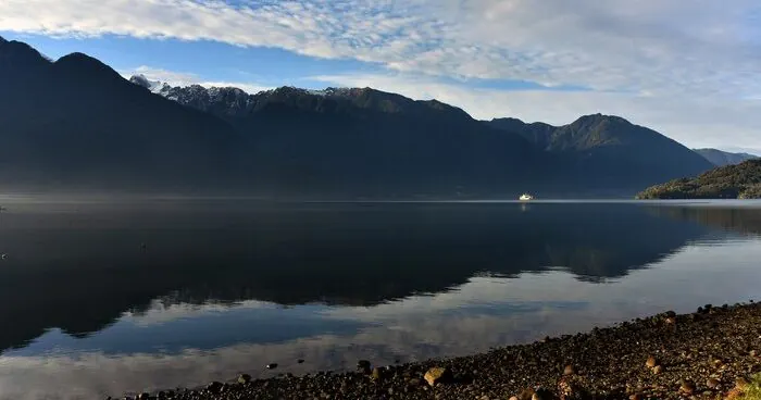 A lake below snow-capped mountains, with green slopes reflected in the water