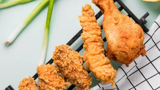 Morceaux de poulet frit sur une grille à côté de ciboules fraîches.