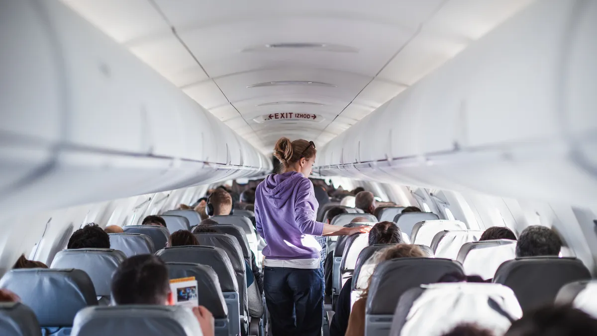 A traveller walking down the aisle of an airliner cabin between rows of seated passengers