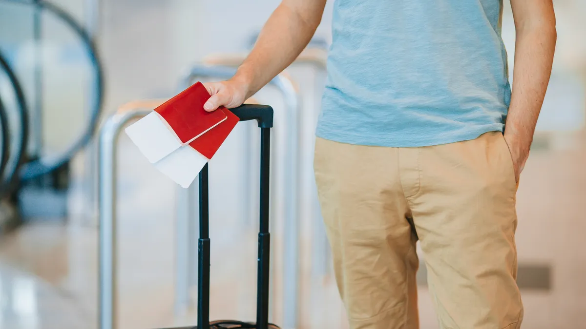 A traveller holds two passports and boarding passes beside a wheeled suitcase.