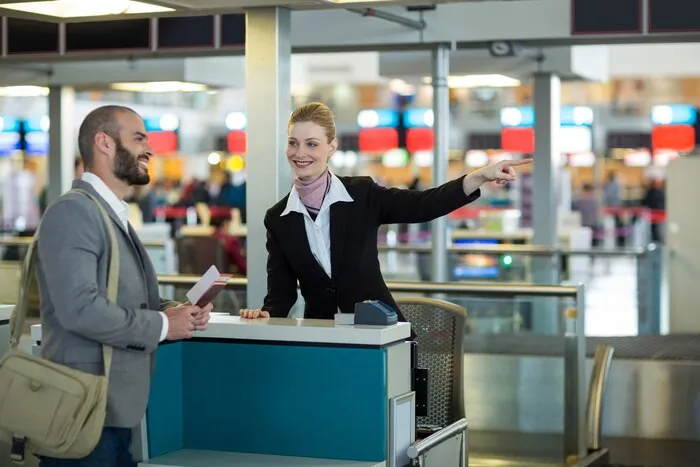 航空会社のチェックインカウンターで、係員がパスポートを持った旅行者に行き先を案内している。