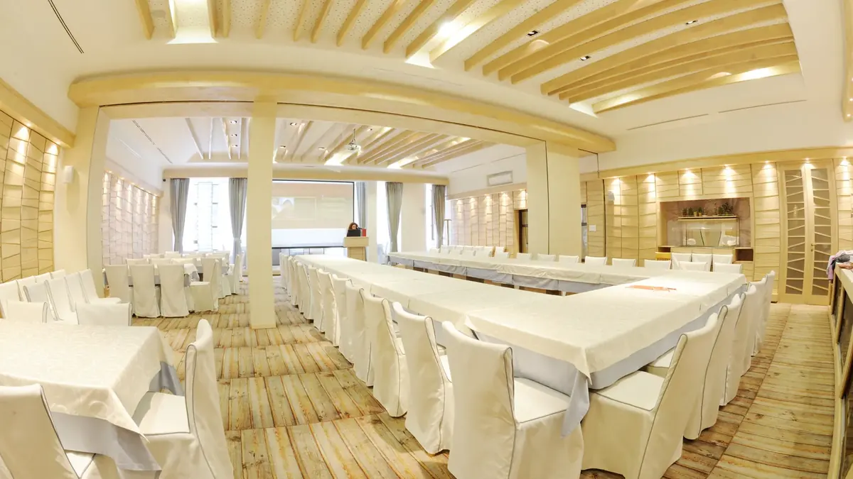 An empty meeting room with tables in a U-shape facing a screen.