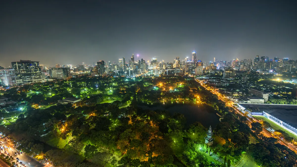 La skyline de Bangkok la nuit, vue à travers les arbres et le lac du parc Lumpini