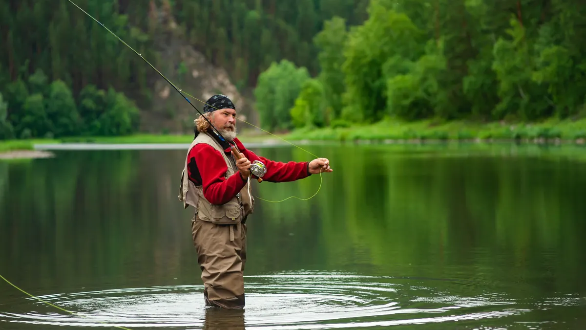 An angler in waders casting a fly line in a calm river
