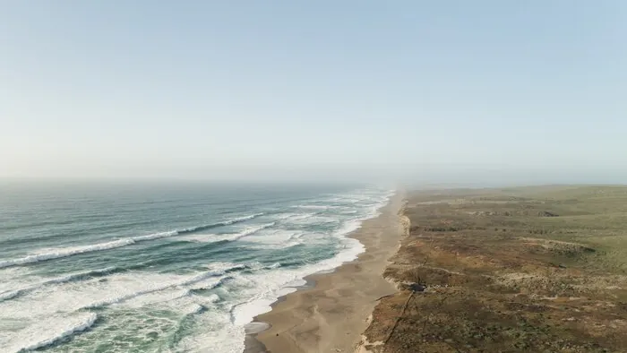 A long sandy shore with surf on one side and low dunes and scrub on the other.