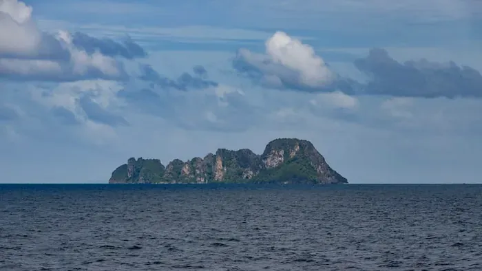 Un pequeño islote rocoso frente a la costa bajo un cielo nublado: los programas en las islas dependen de los ferris y del tiempo.